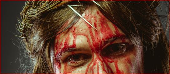 Jesus eyes with fixed gaze while face os streaked with blood and wearing a grown of thorns