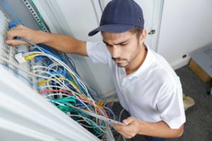 Electrician examines an electrical panel with colorful cables.