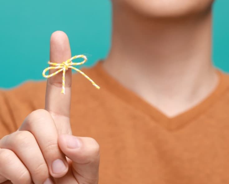 Hand with pointed index finger wrapped with a yellow cord tied in a bow.